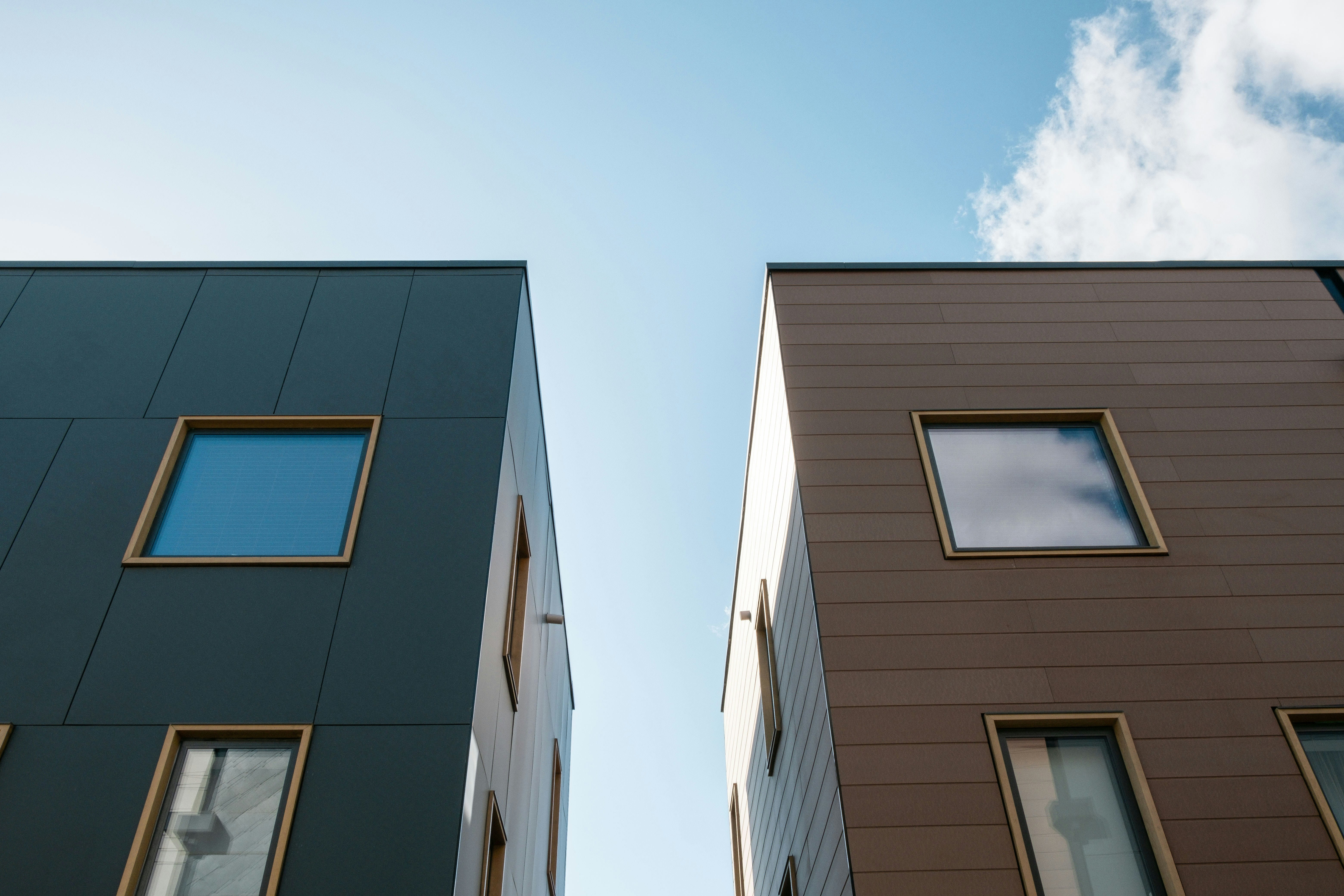View looking up at two modern buildings with square windows and clear blue sky between them.