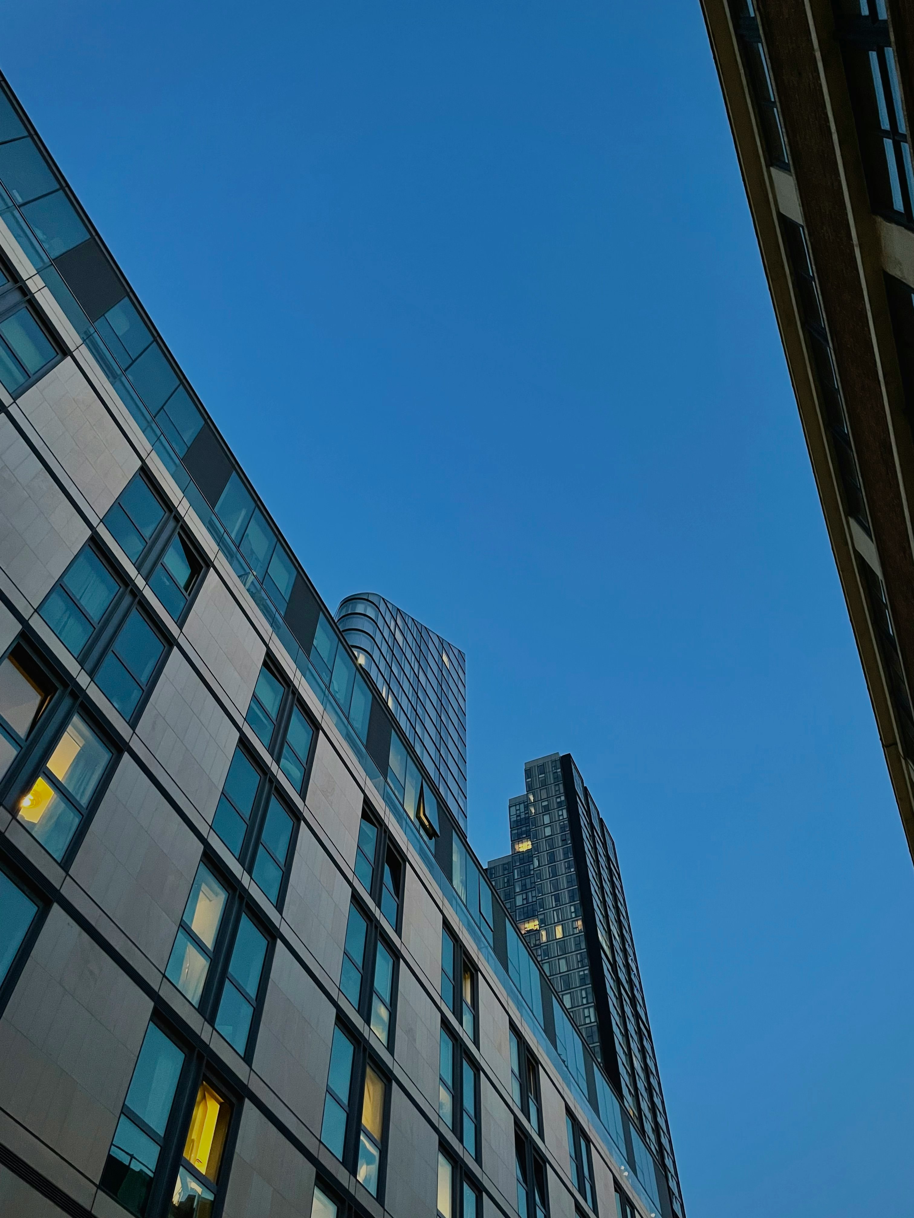 Low-angle view of modern high-rise buildings under clear blue evening sky.