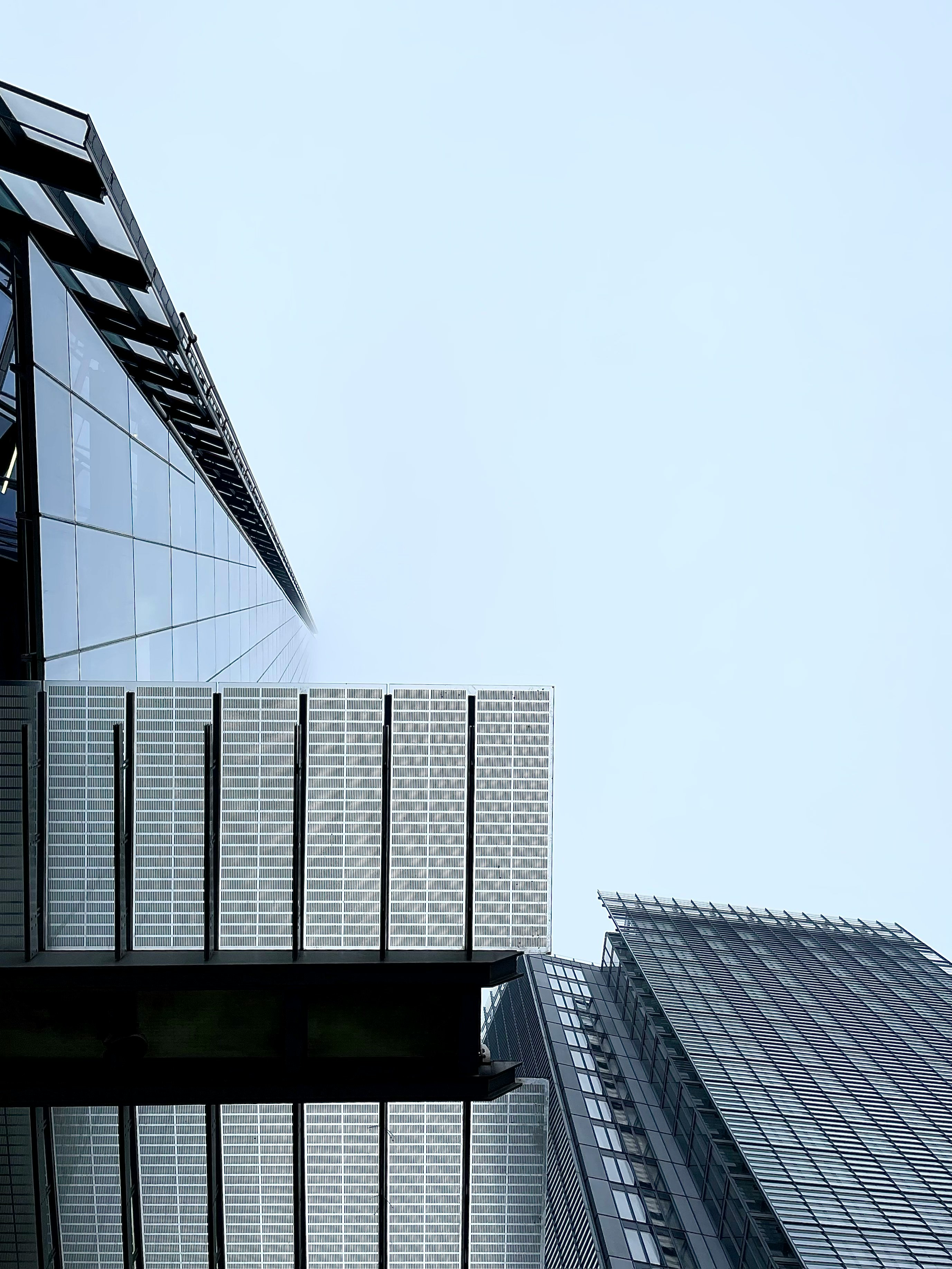 Looking up at modern glass skyscrapers and solar panel structures against a pale blue sky.