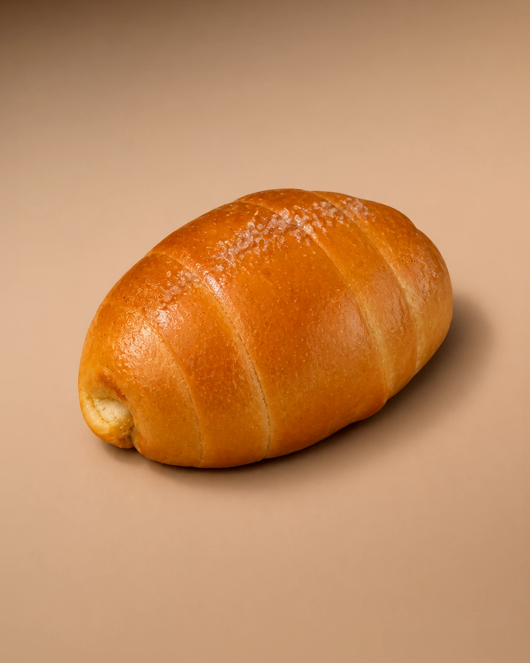 Signature salt bread from Salted, a glossy golden Korean-style shio pan roll with coiled seam ridges and coarse salt crystals scattered across the crown.