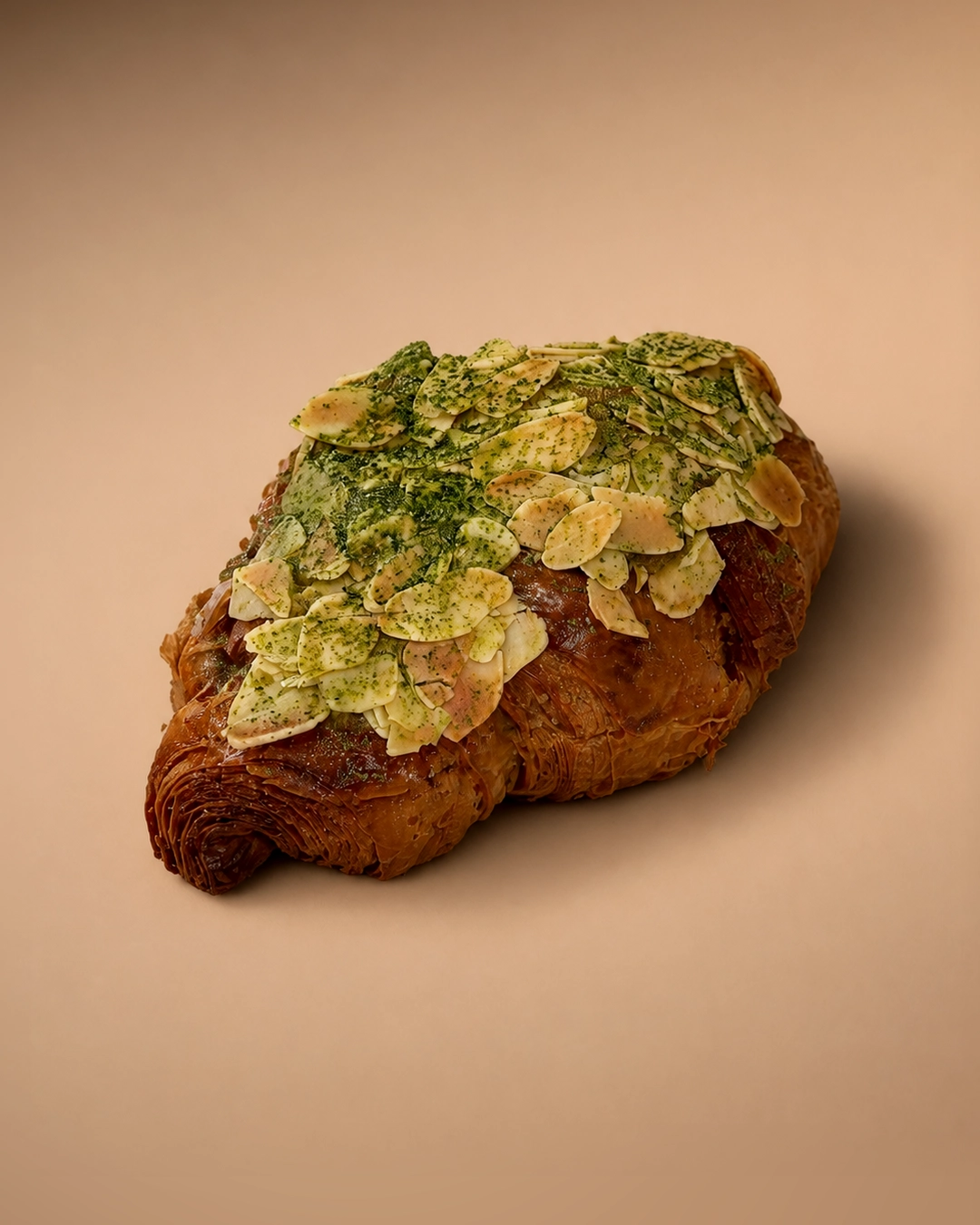 Matcha almond croissant, a laminated croissant covered in flaked almonds and dusted heavily with bright green matcha powder.