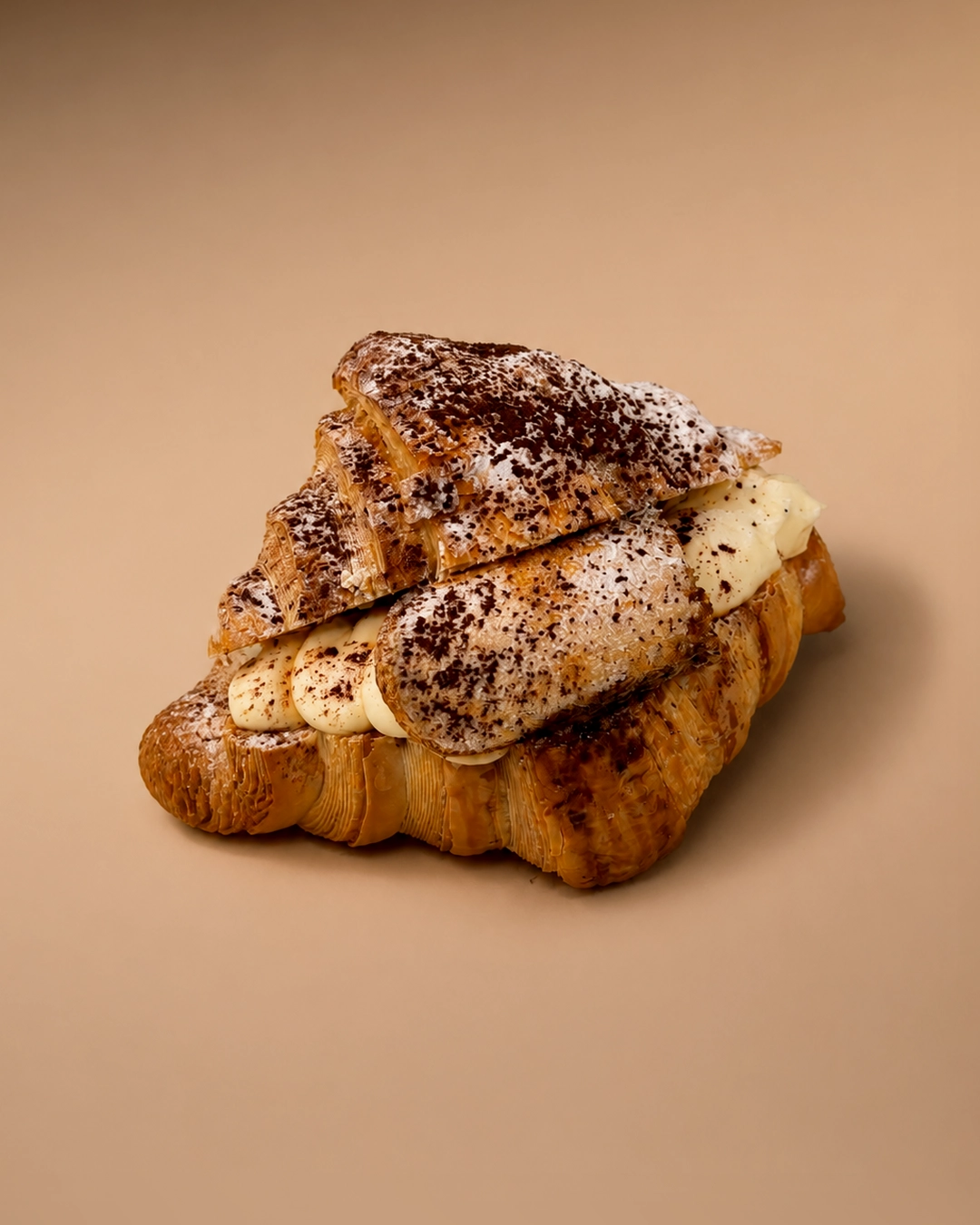 Tiramisu croissant, split and filled with a row of piped mascarpone rosettes, the top half dusted with cocoa powder and icing sugar.
