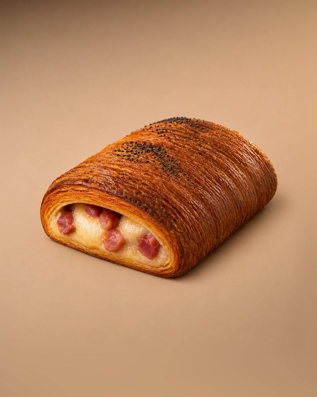 Pastrami and provolone croissant, a wide laminated block cut open to show melted provolone and pieces of pastrami, its top scattered with poppy seeds.