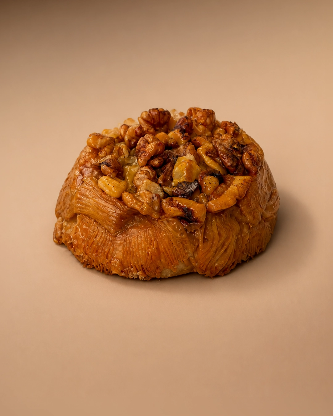 Walnut butterscotch croissant, a round flat laminated pastry lacquered in amber butterscotch and piled with caramelised walnuts.