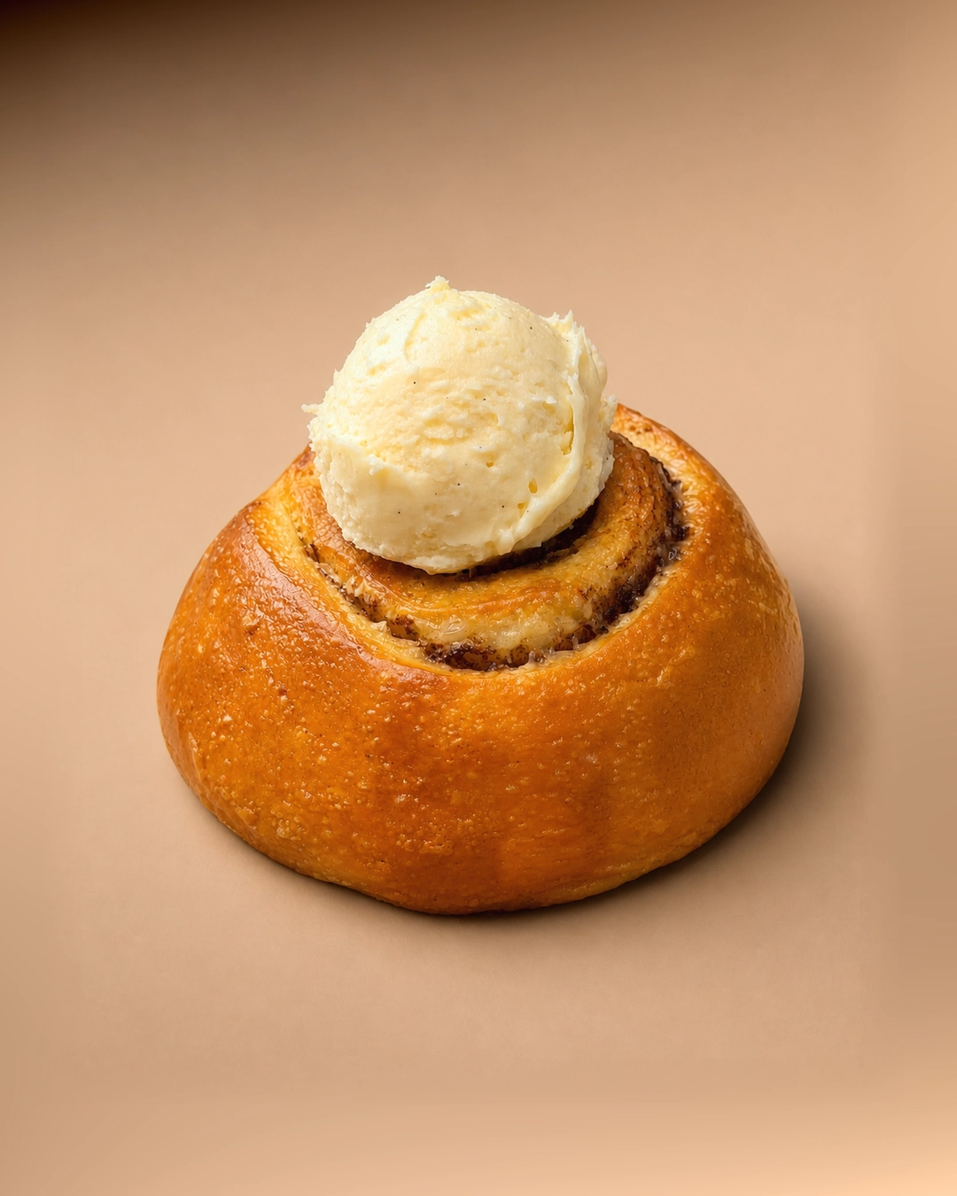 Cinnamon scroll, a glossy golden spiral bun with a single scoop of vanilla-flecked butter cream softening in the centre.