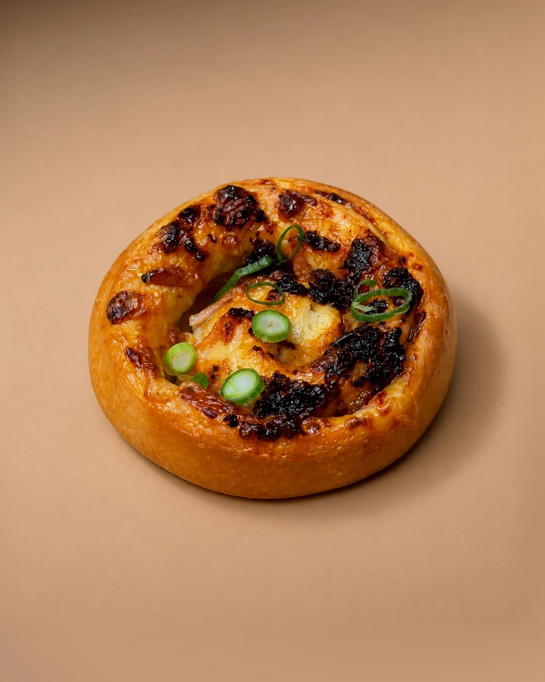 Chilli maple bacon scroll, a golden spiral bun loaded with crisped bacon, melted cheese and maple glaze, scattered with sliced spring onion.