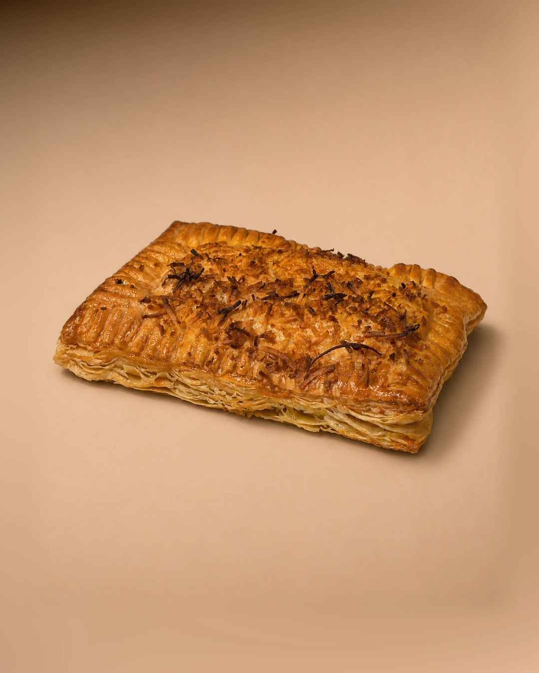 Beef rendang puff pastry, a sealed rectangular parcel with a crimped border and splayed lamination, topped with crispy fried shallot.