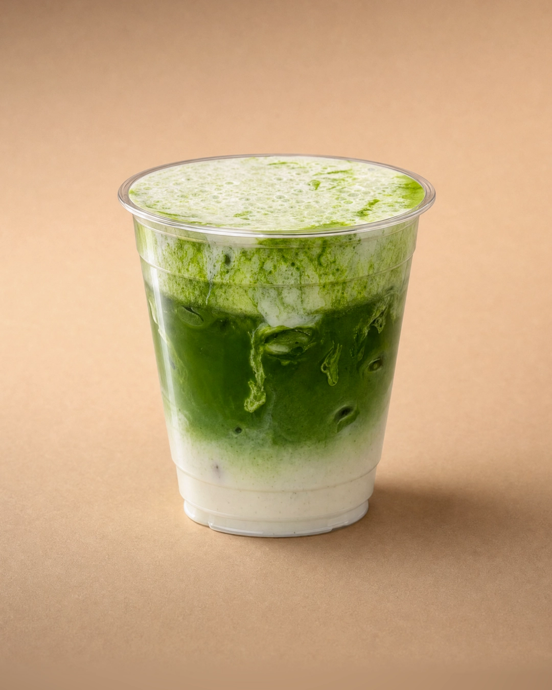 Salted matcha latte, bright green matcha streaking down through white milk and ice, under a thin, bubbly layer of salted cold foam with green showing through.