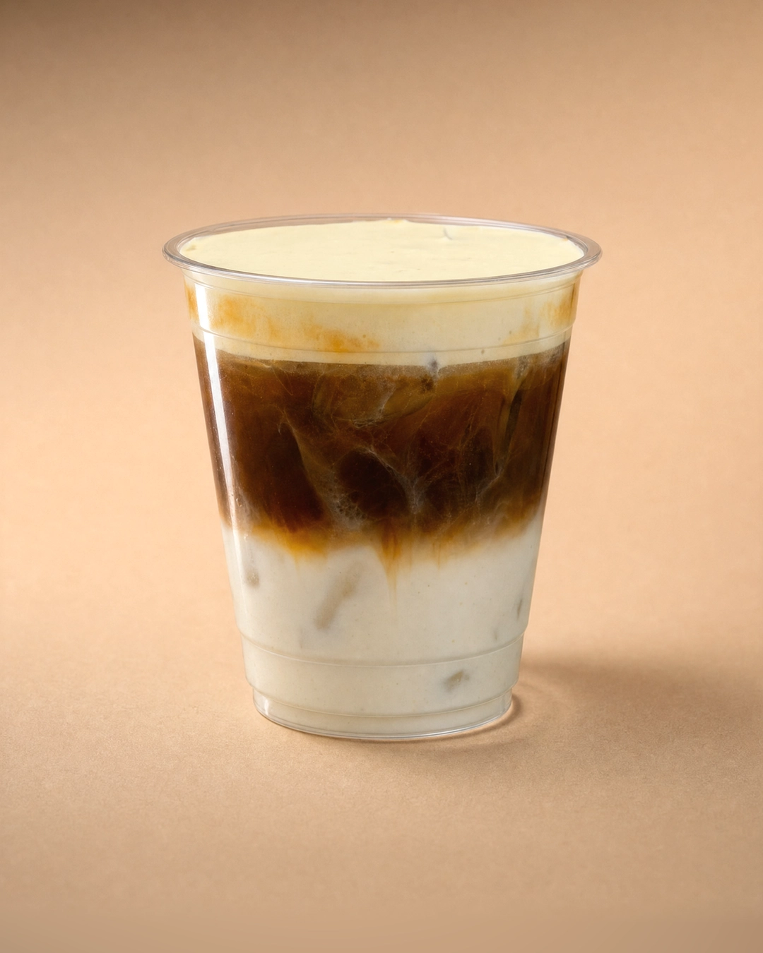 Salted coffee latte, white milk and ice at the base with dark espresso bleeding down into it, under a smooth, level cap of pale salted cold foam.