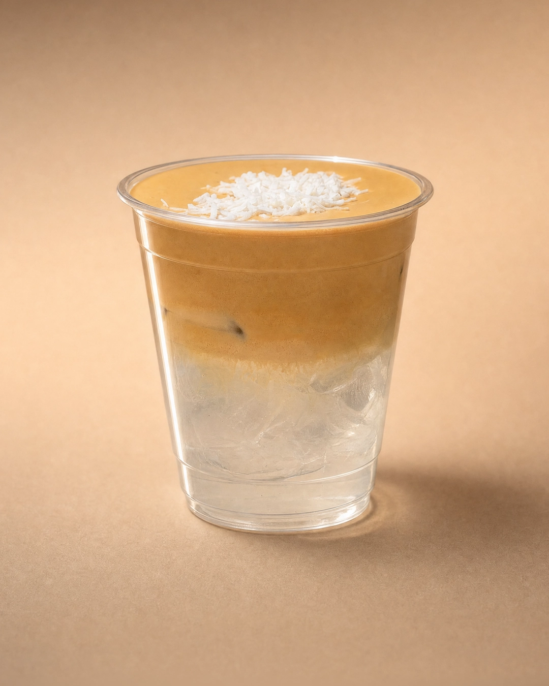 Coconut coffee cloud, clear coconut water and ice filling the lower half of the cup, under a thick caramel-tan coffee cold foam with shredded coconut in the centre.
