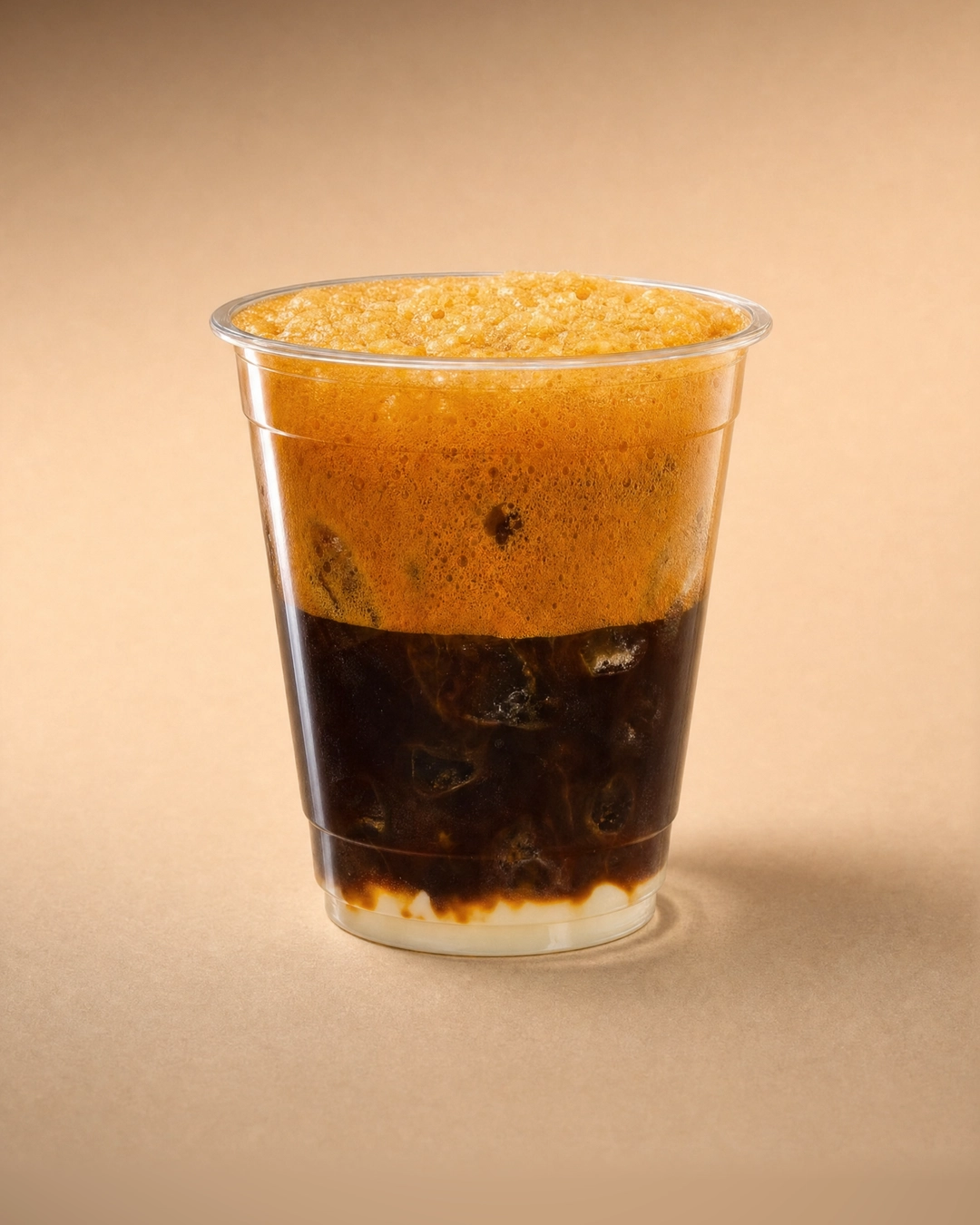 Nâu (iced coffee), a deep column of near-black coffee and ice over a thin layer of condensed milk, topped with a thick, bubbly orange crema level with the rim.