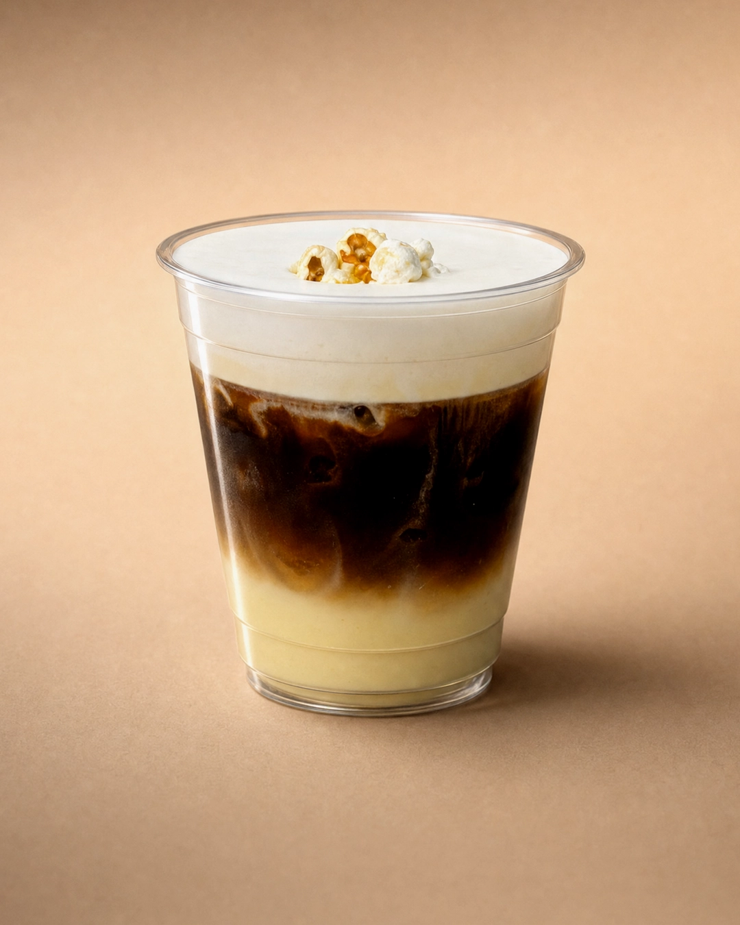 Cà phê bắp (corn coffee), pale yellow corn milk under a band of dark coffee and ice, capped with a smooth cream popcorn cold foam and a small cluster of popcorn.