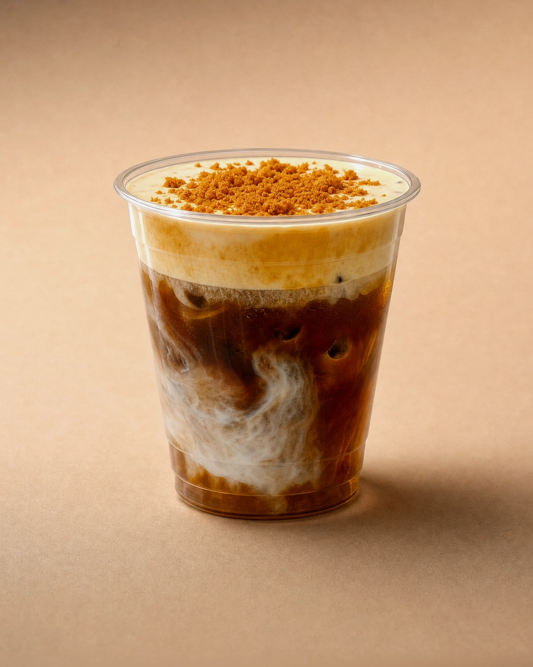 Banana and Biscoff coffee, dark espresso with a pale swirl through it and ice at the wall, under a pale yellow banana cold foam heaped with Biscoff crumb.