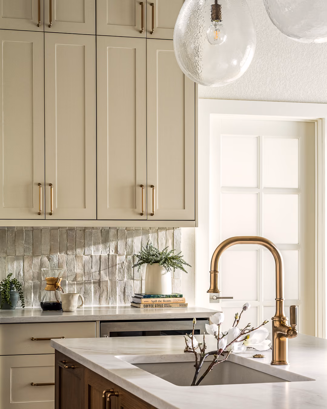 Brass kitchen faucet beneath tall cabinets with a quartz countertop and tiled backsplash