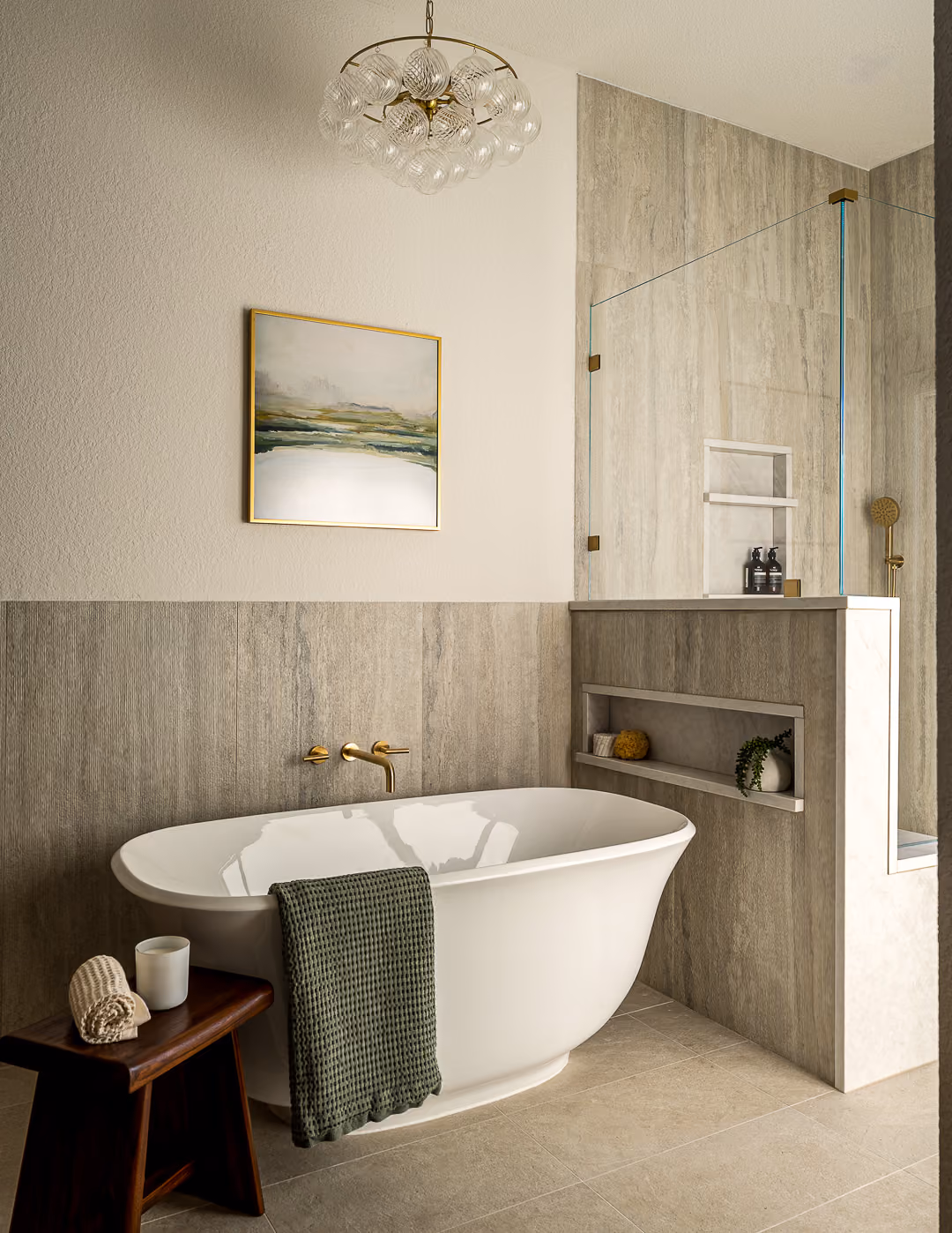 Built-in soaking tub with neutral tile, recessed shelving, and brass fixtures