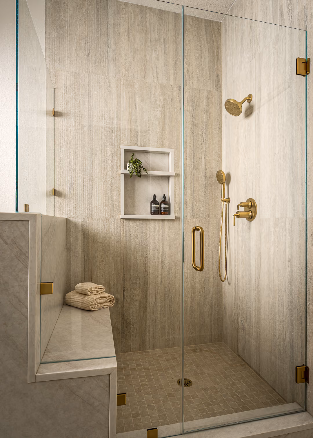 Custom walk-in shower with floor-to-ceiling tile, frameless glass, bench, and niche