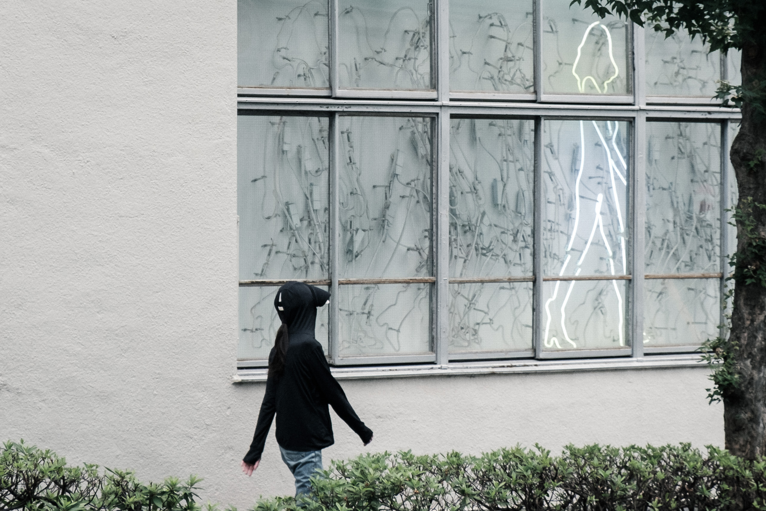 A figure in a black hoodie walks past a window where a neon outline of a woman walks the other way.