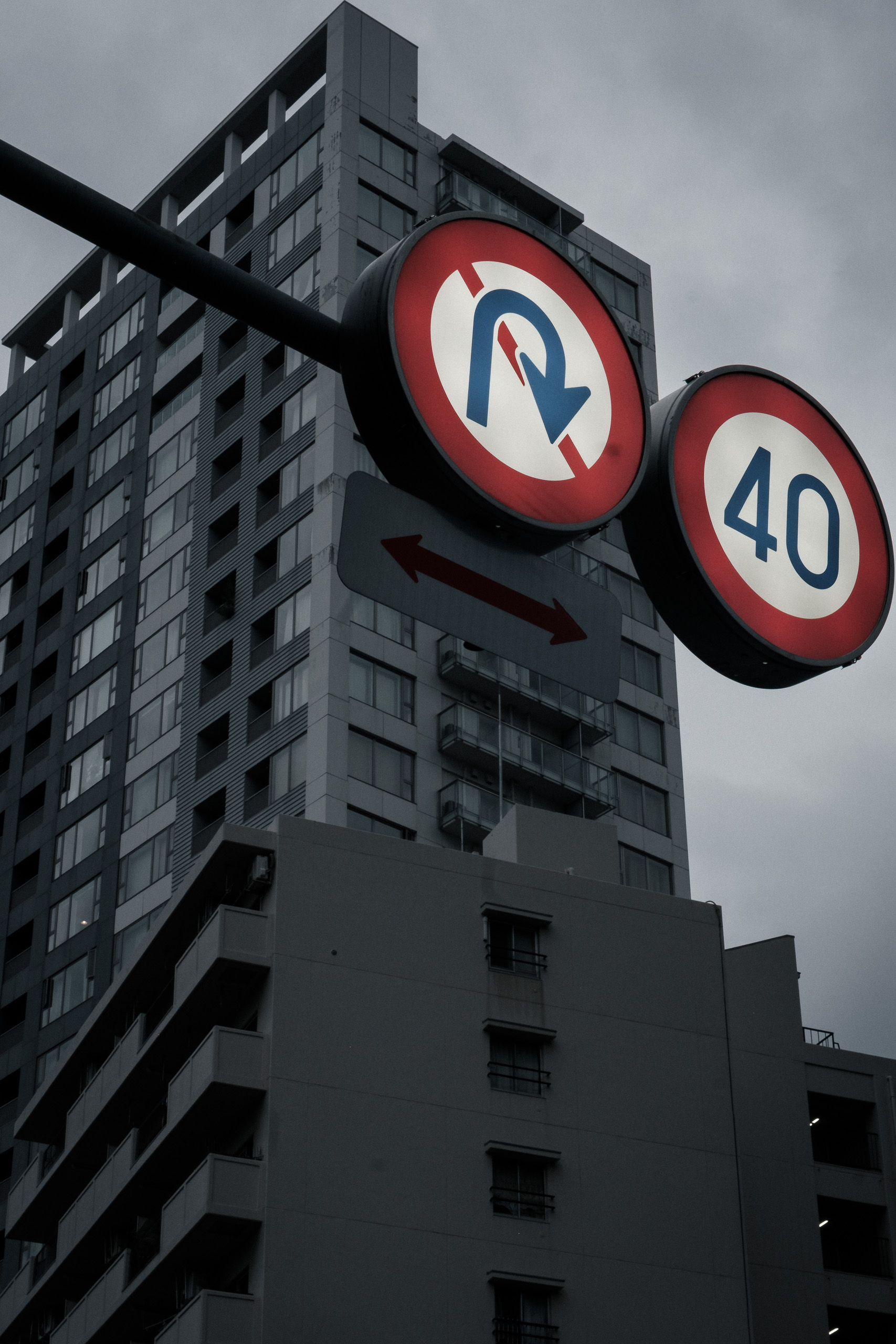 No U-turn and 40 speed limit signs against a dark apartment tower and grey sky.