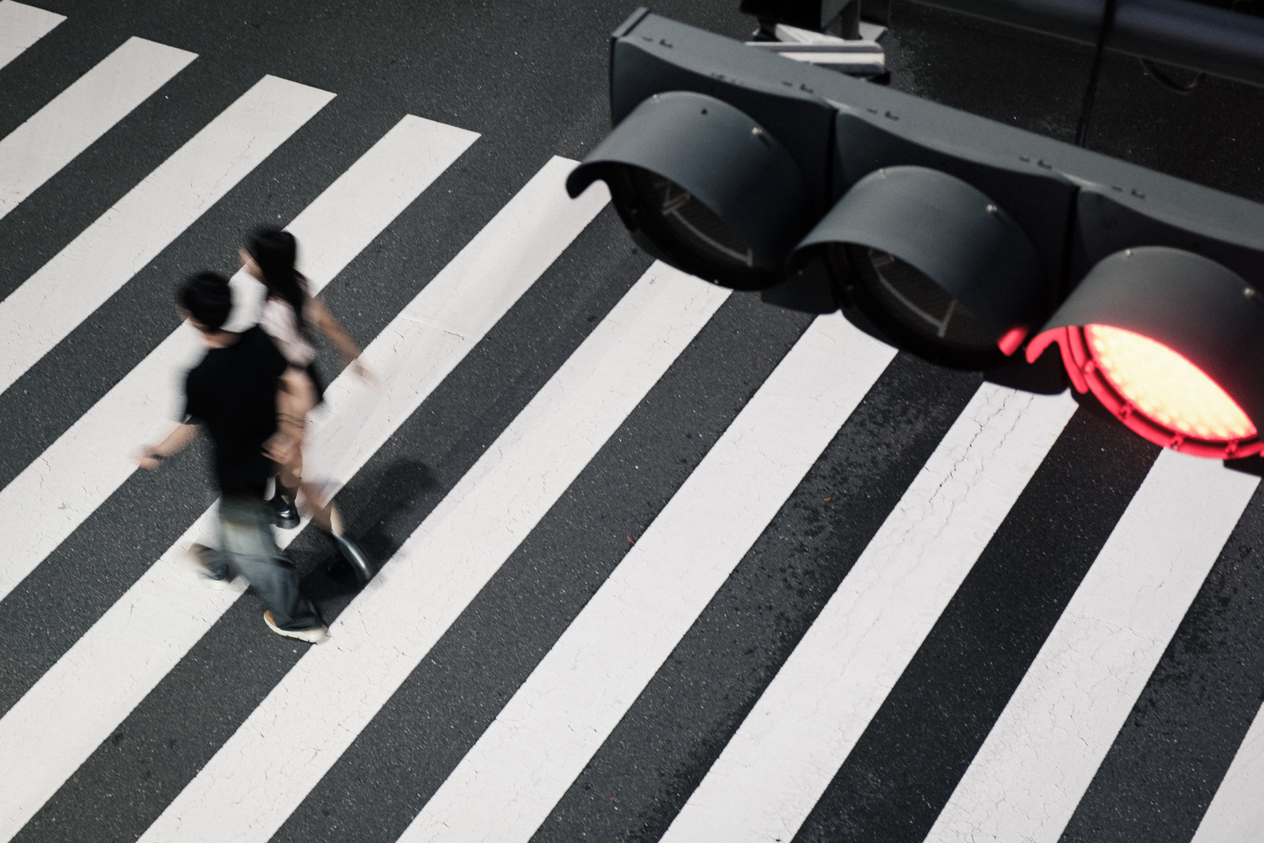 Two people cross a zebra crossing beneath a red traffic light, seen from above.