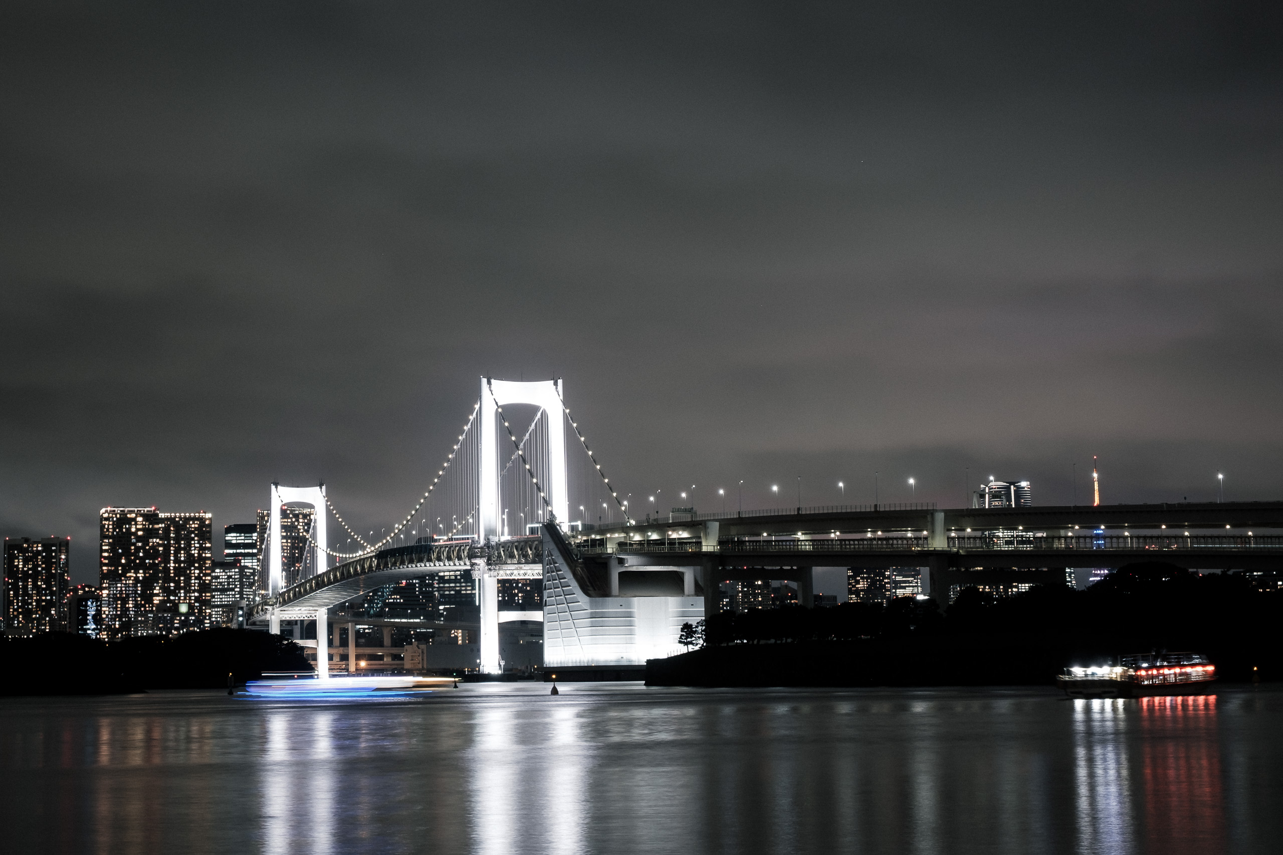 The Rainbow Bridge lit at night and reflected in the bay.