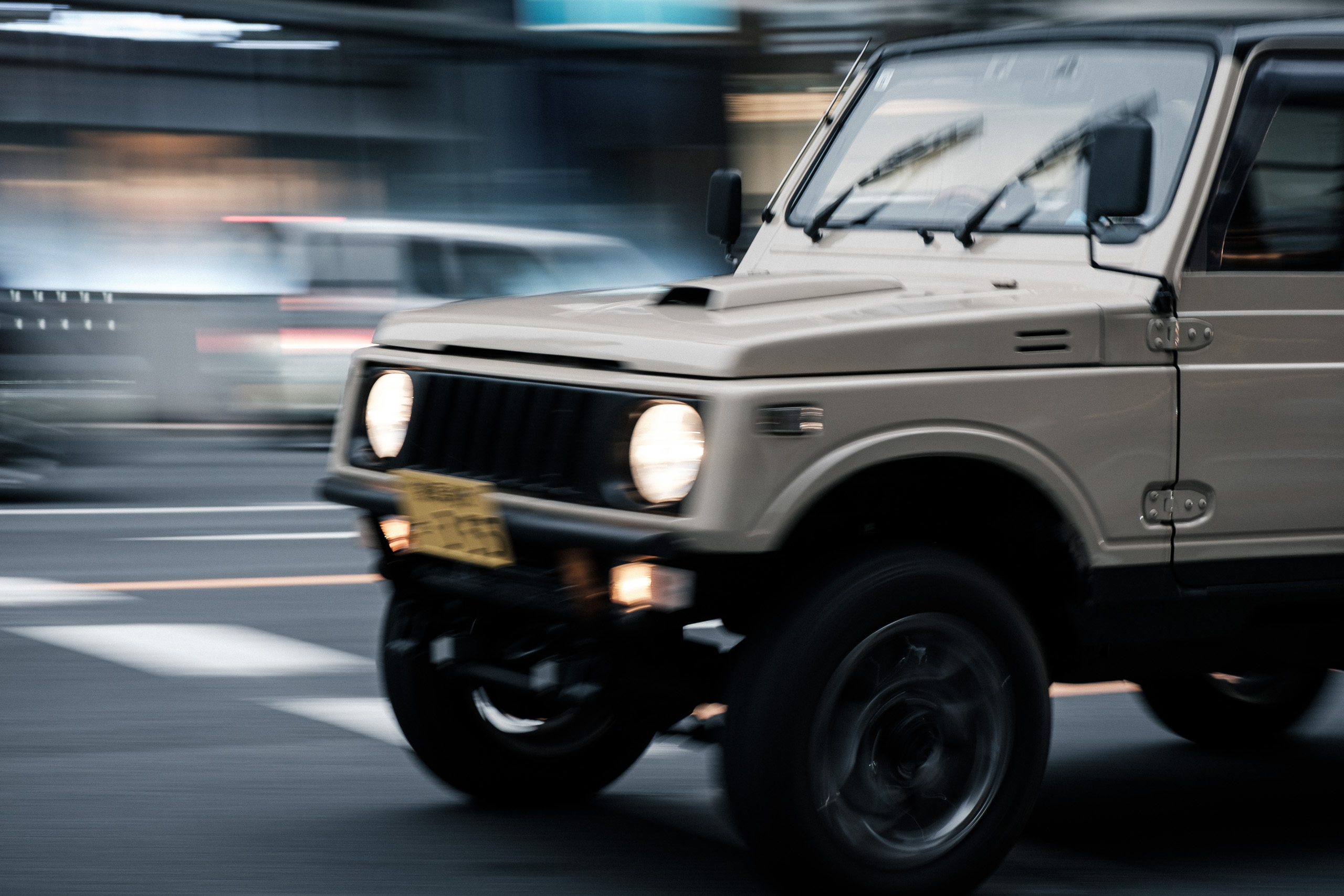 A beige off-road vehicle in motion, the street behind it blurred into streaks.