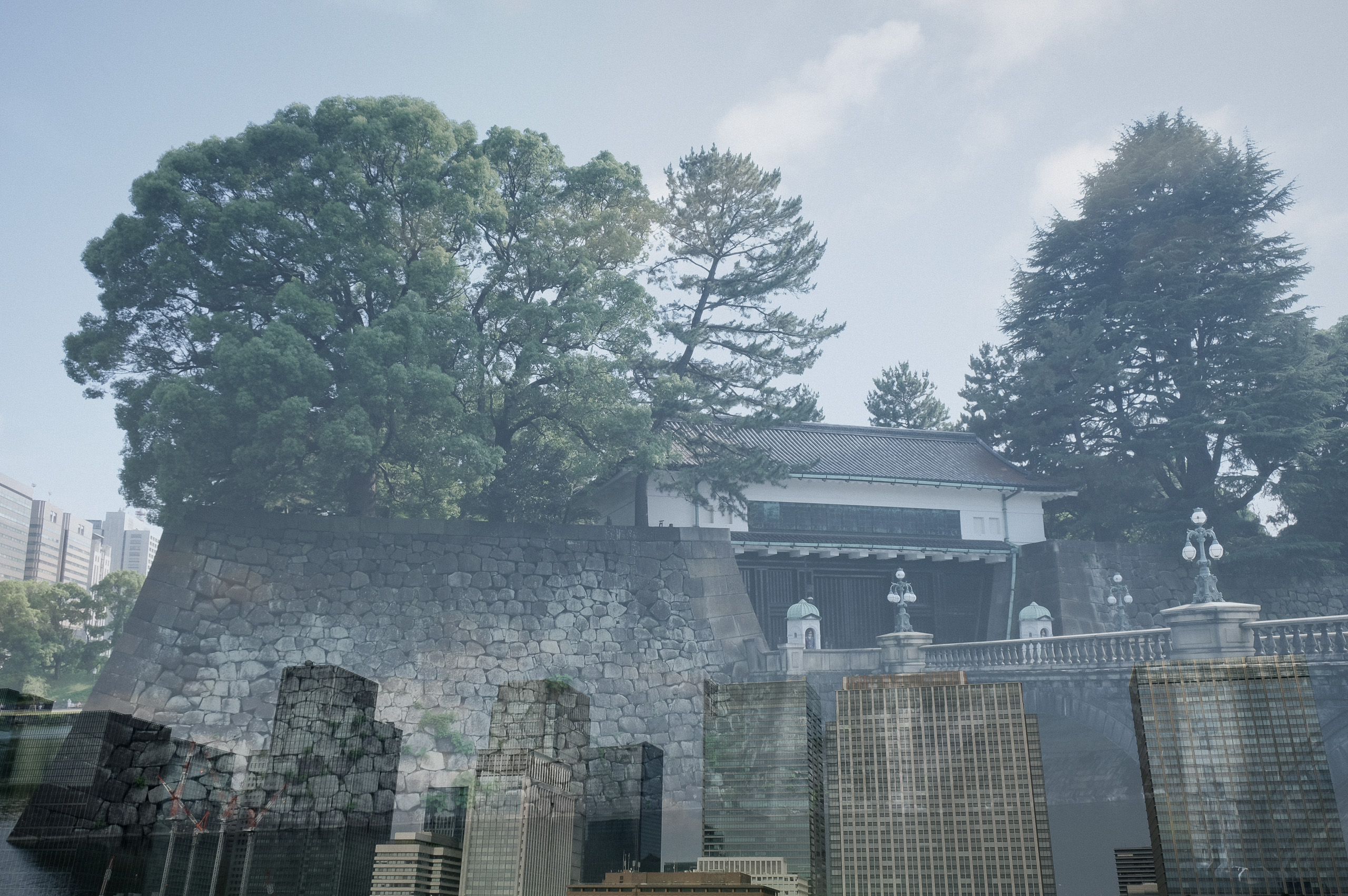 Multiple exposure of a palace gate and stone wall layered with office towers.