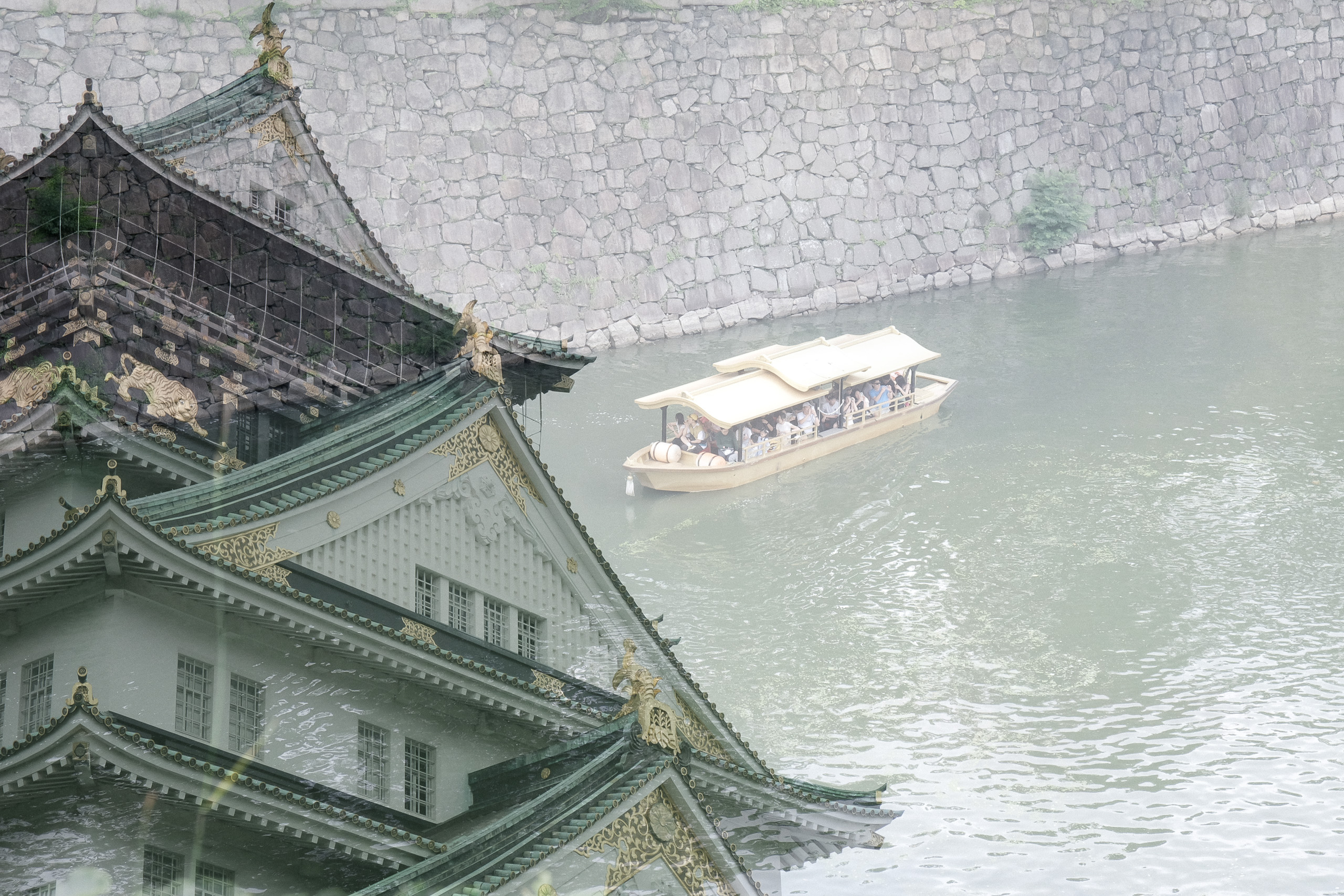 Multiple exposure of a castle roof layered over a moat with a tourist boat.