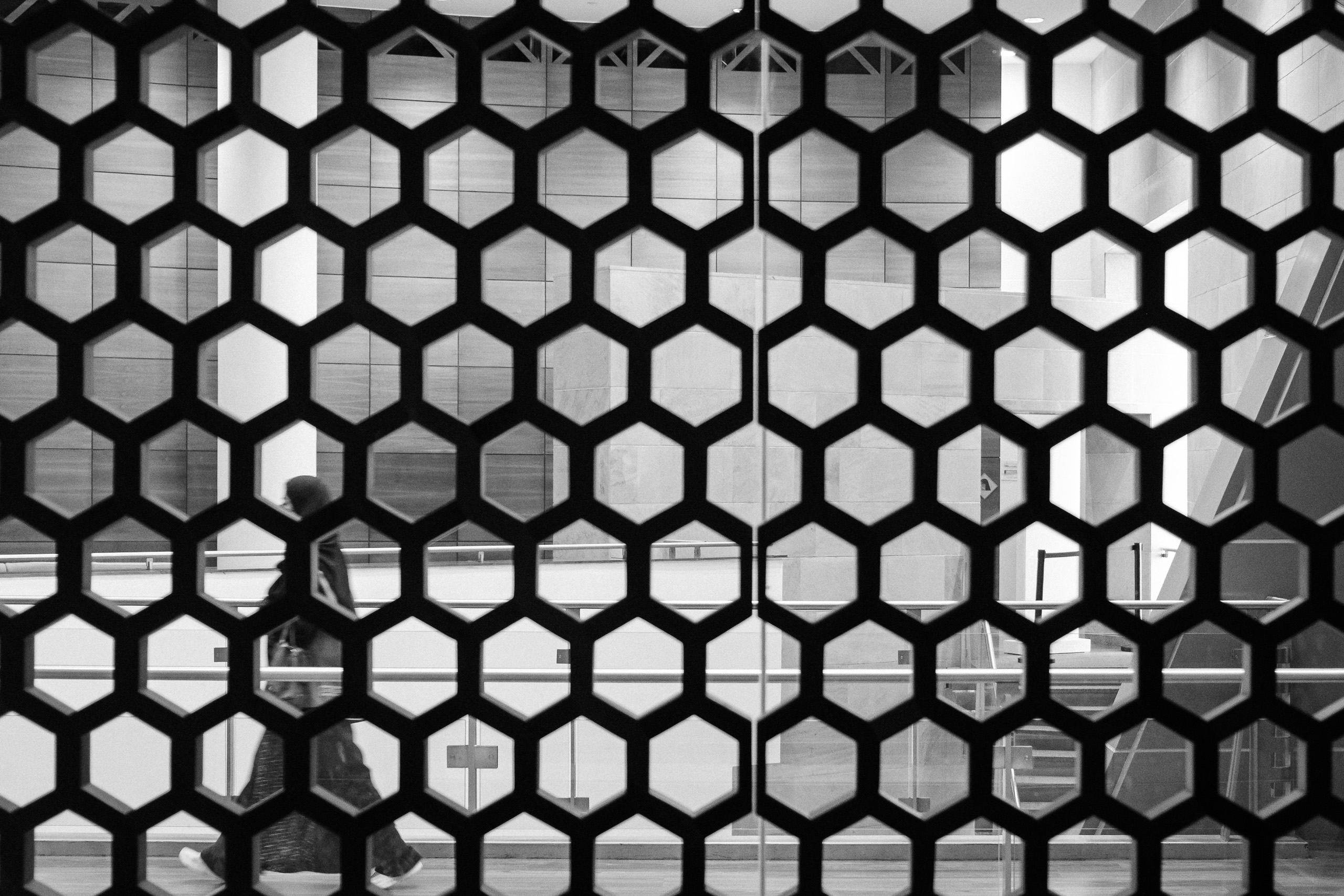 Black hexagonal lattice screen with a blurred figure walking behind it, black and white, Saudi Arabia