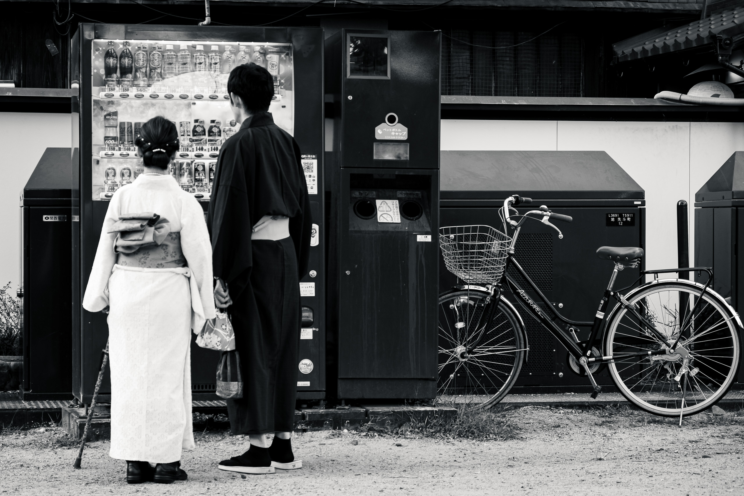 A couple in kimono stand with their backs to the camera before a lit vending machine in Pontocho, Kyoto.