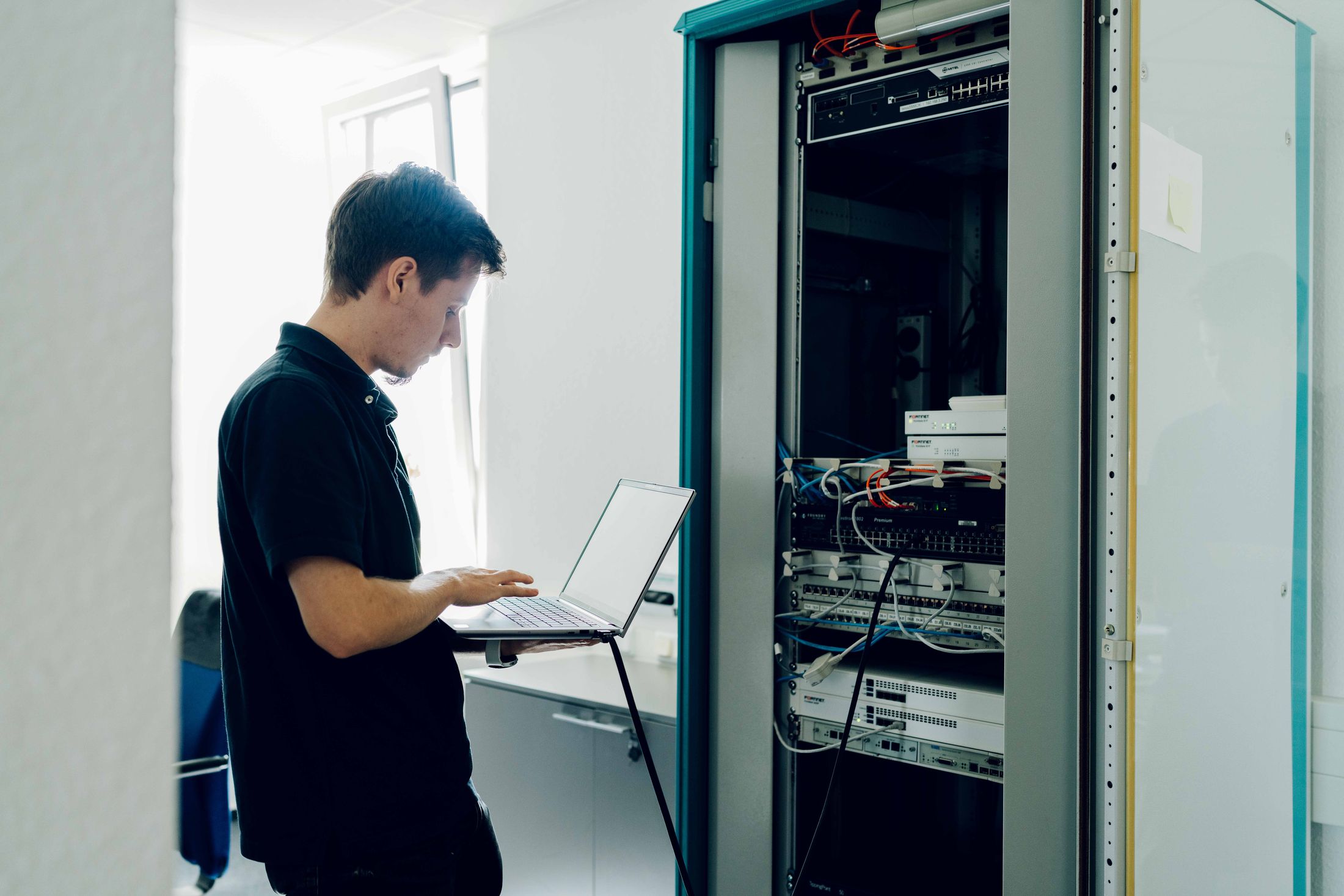 Techniker mit Laptop am Serverschrank bei der Wartung