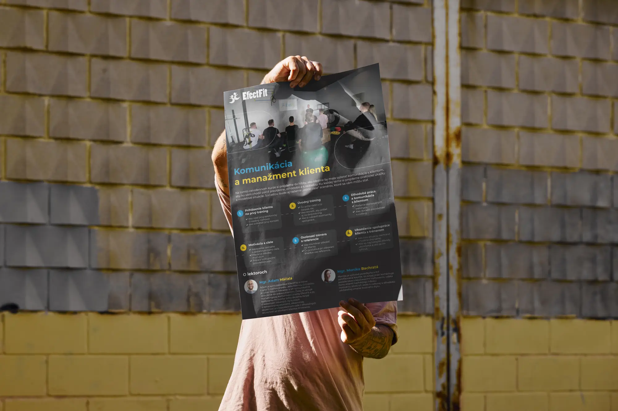 A hand holding up a printed EfectFit poster against a brick wall