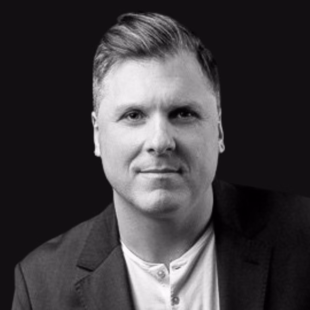 Black and white portrait of a middle-aged man with short hair wearing a light-colored shirt and dark blazer, looking directly at the camera with a neutral expression.