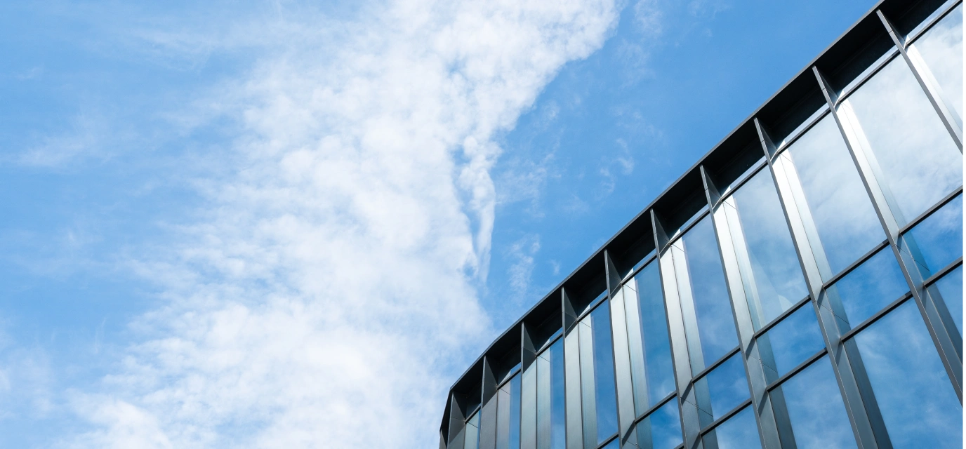 Modern glass building facade reflecting a blue sky with scattered white clouds.