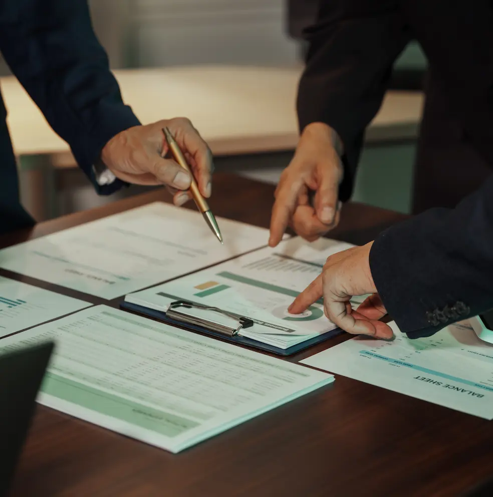 Two professionals reviewing financial documents and pointing at figures on a balance sheet.