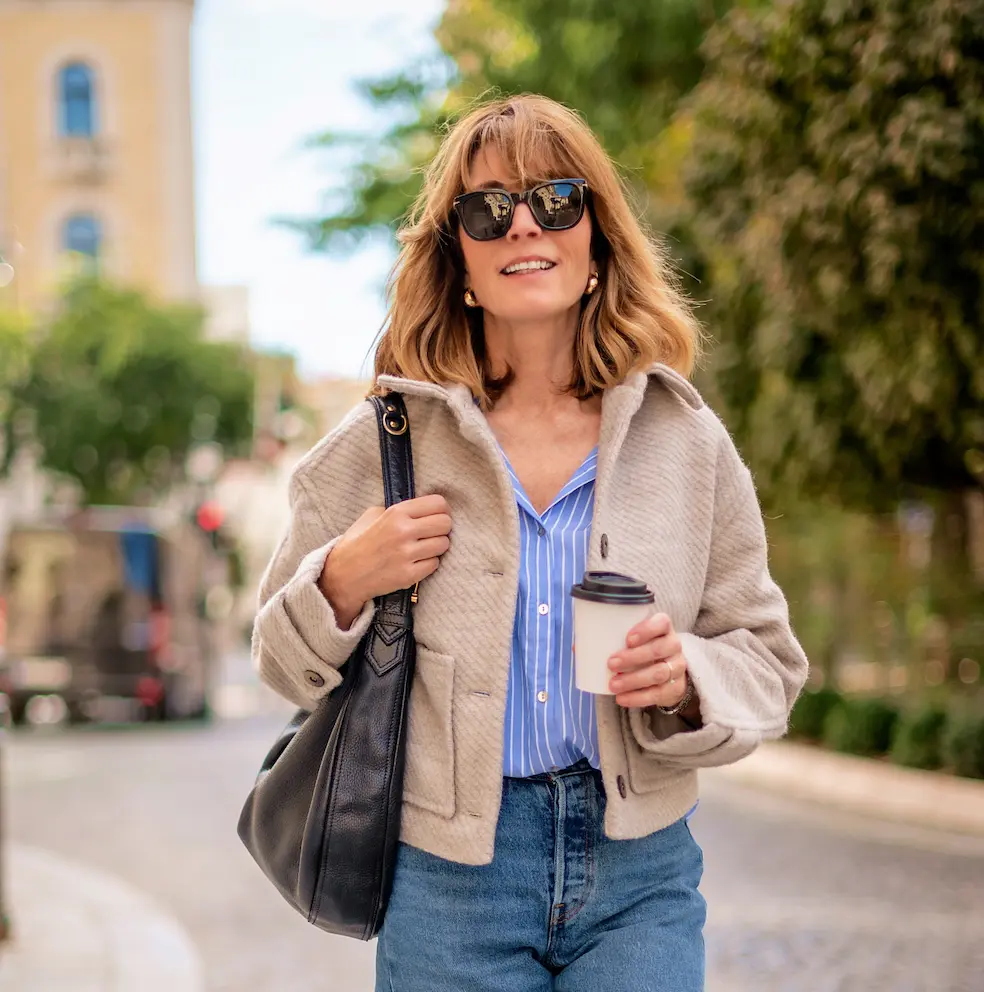 Woman in a coat walking outdoors while holding a coffee cup.