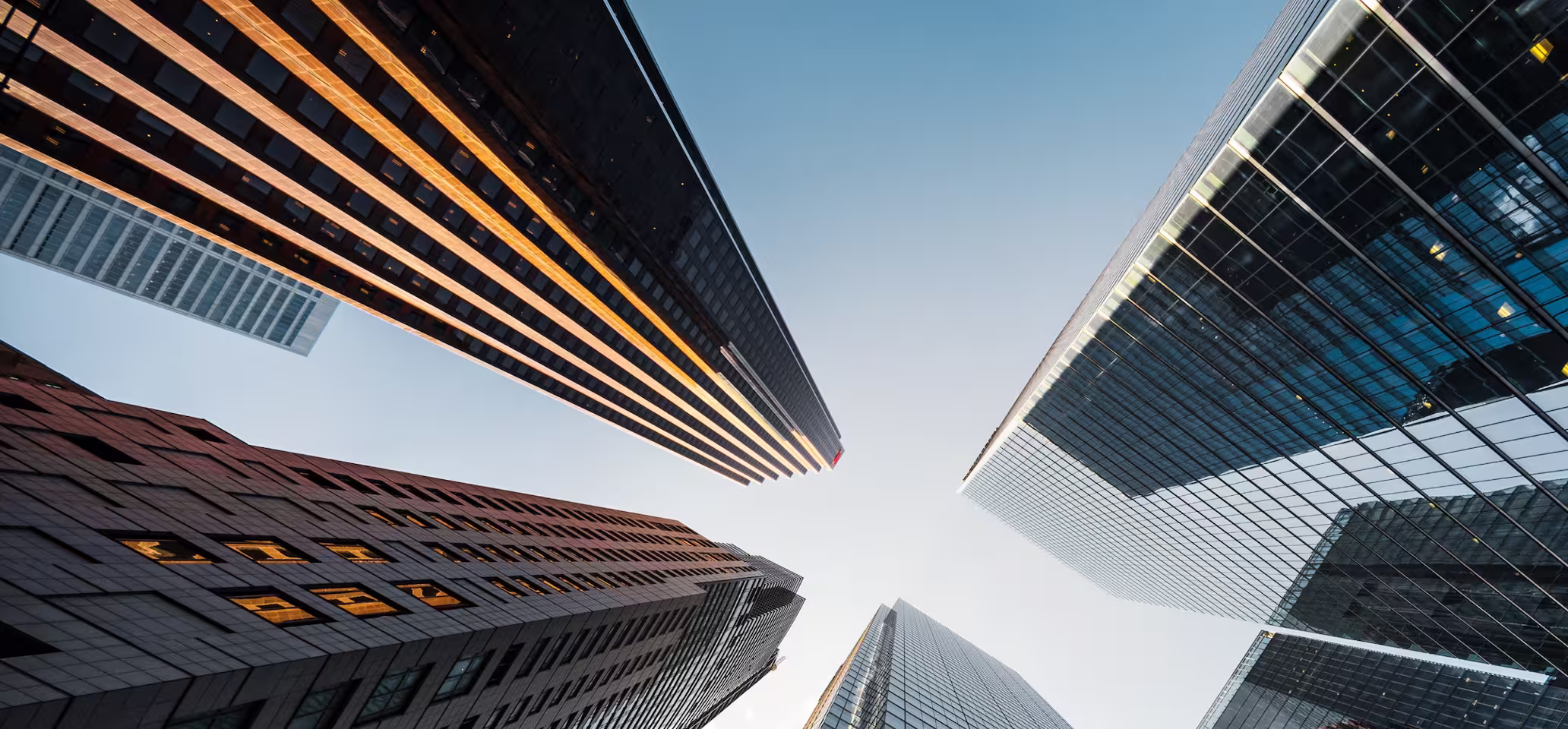 View looking up at modern city skyscrapers against a clear blue sky.