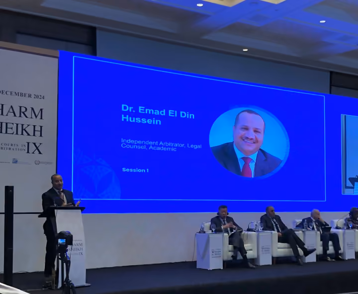 Dr. Emad Hussein speaking at an international arbitration conference, with his profile displayed on the presentation screen.