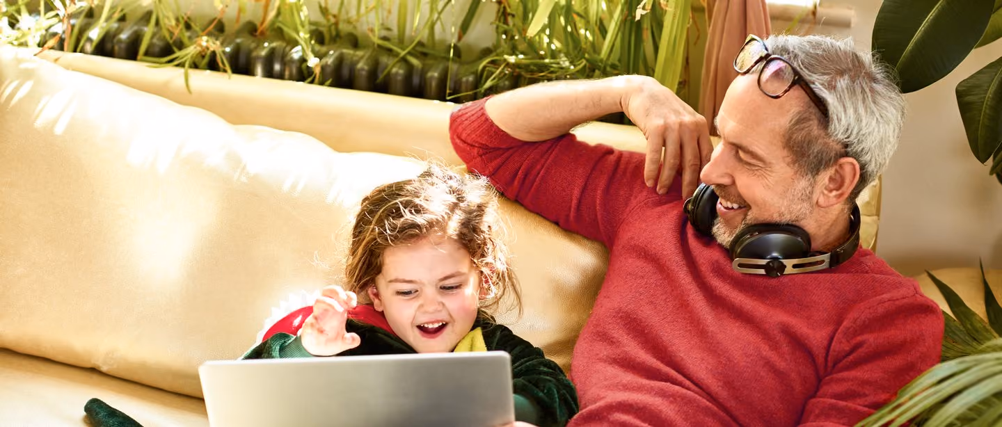 Far og datter ser på laptop i sofaen