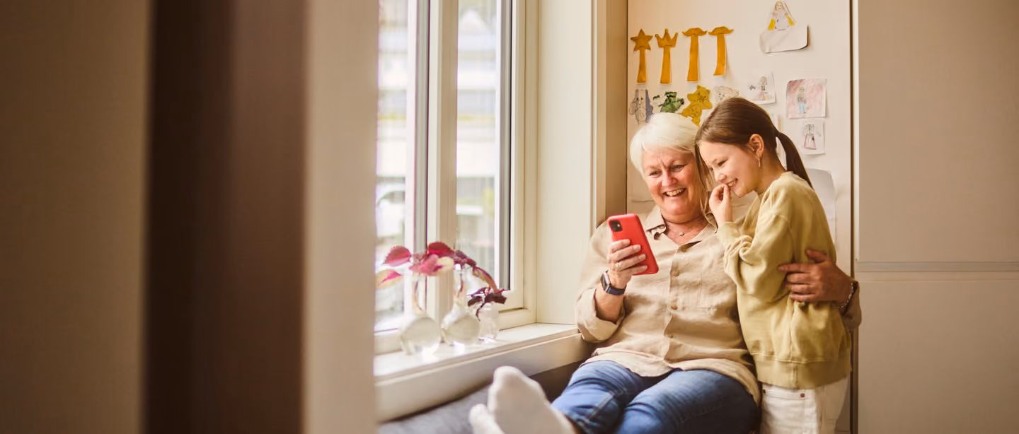 Bestemor og barnebarn ser på mobil i vinduskarmen