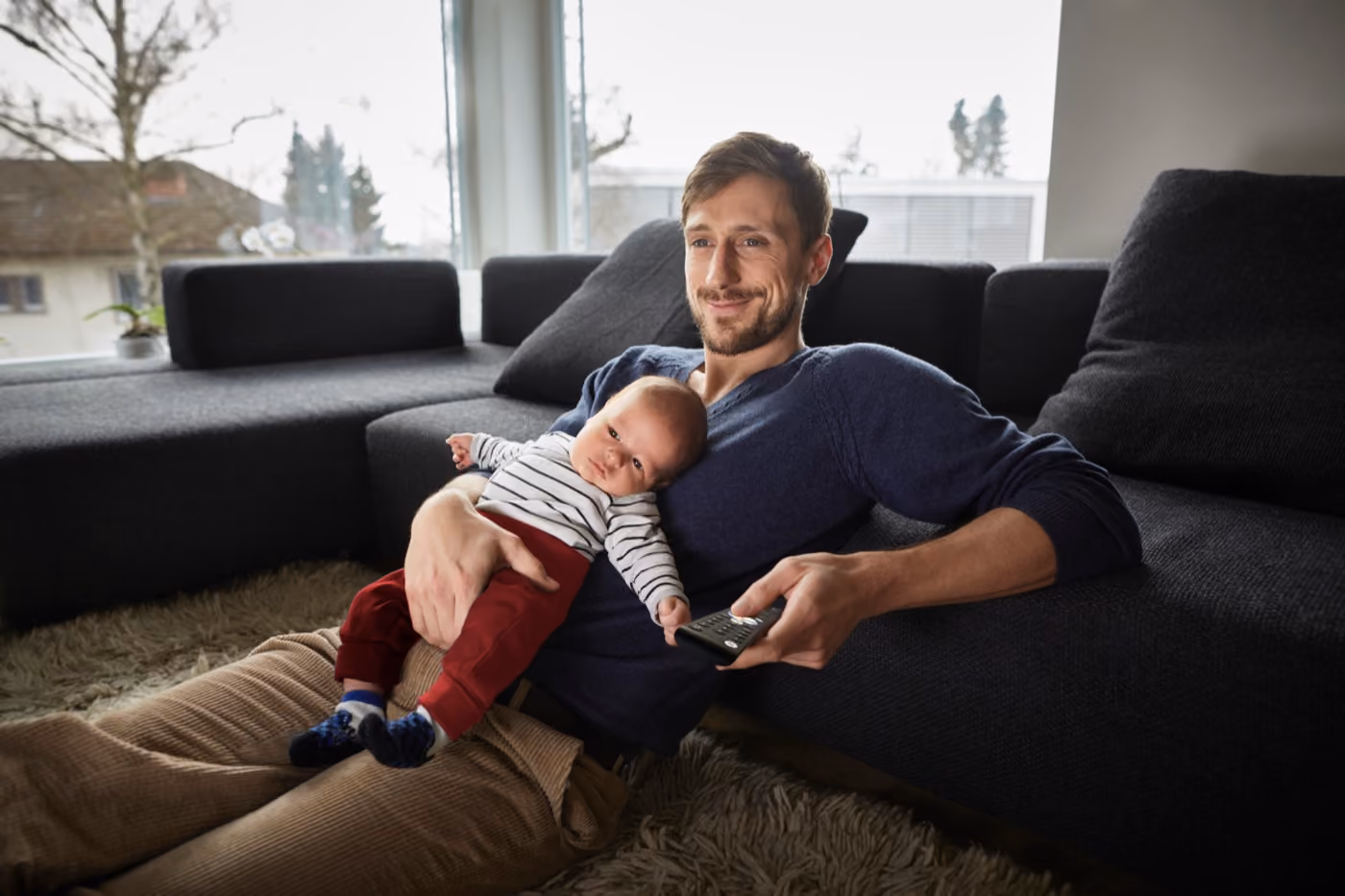 Far ligger i sofaen med babyen sin og ser på TV