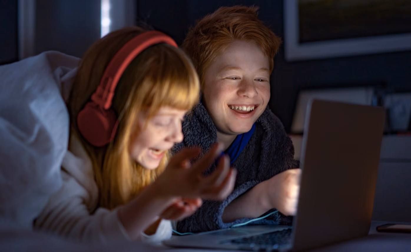 To barn ser på film på en laptop i senga på hytta
