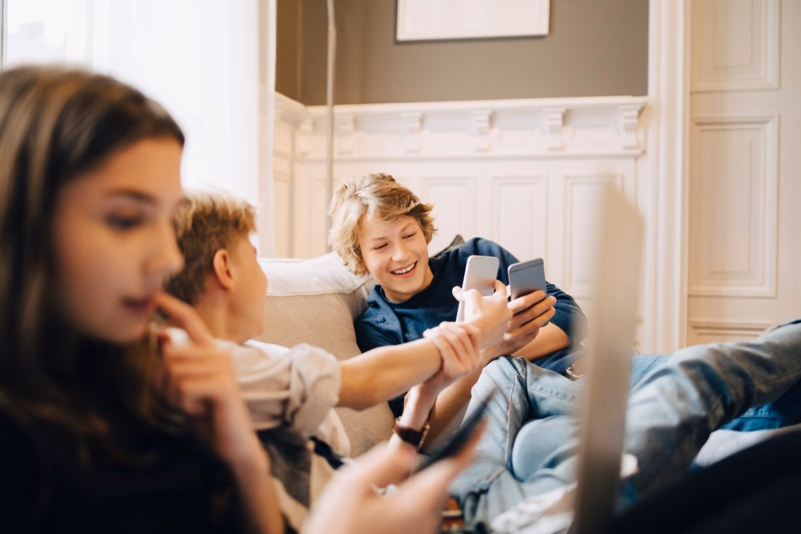 Tre barn ser sammen på mobil og nettbrett i sofaen hjemme