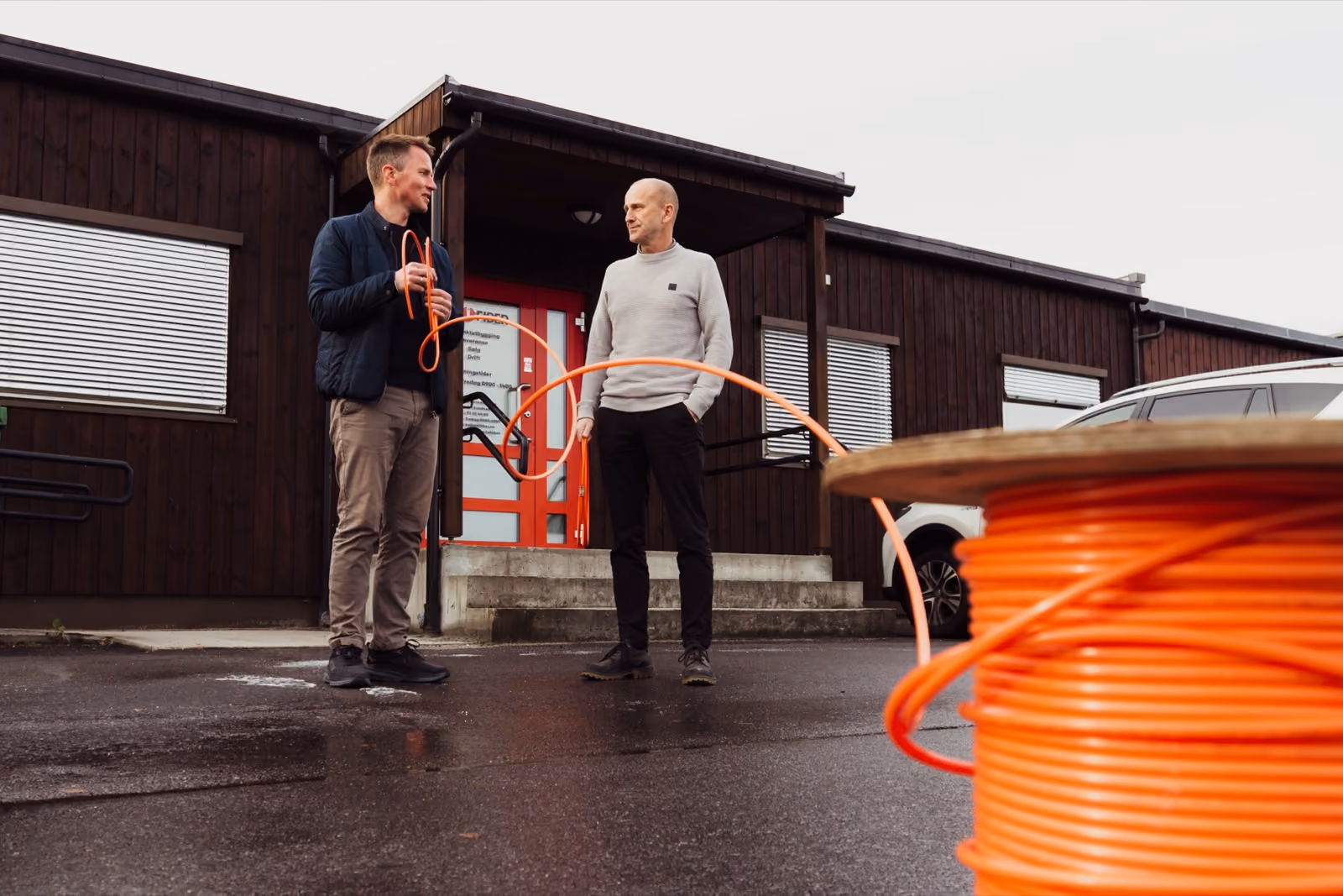 To menn utenfor et bygg med en trommel med oransje fiberkabel