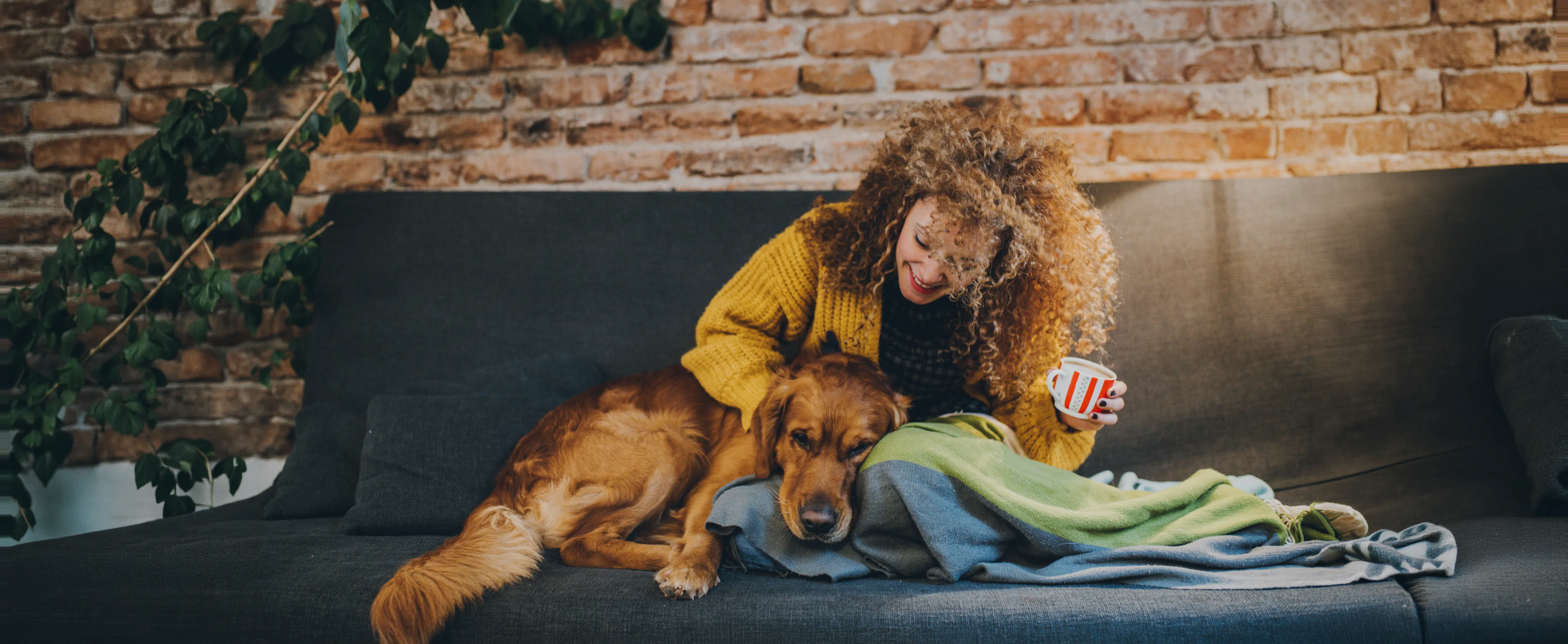 Kvinne koser med hunden sin i sofaen hjemme