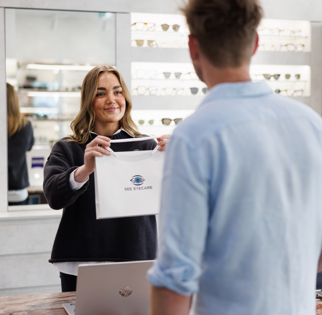 An image of a See Eyecare staff member handing new glasses to a customer