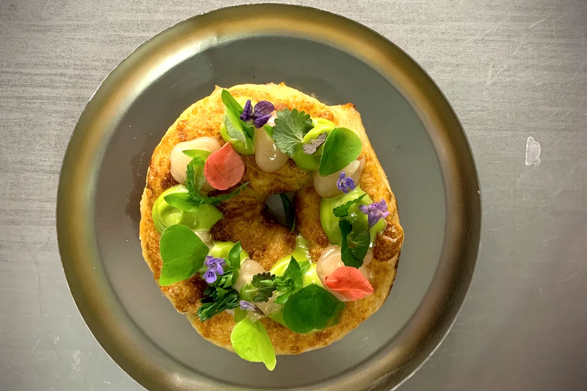 Gebackener Teigring mit Kräutersauce, Perlzwiebeln und essbaren Blüten, von oben