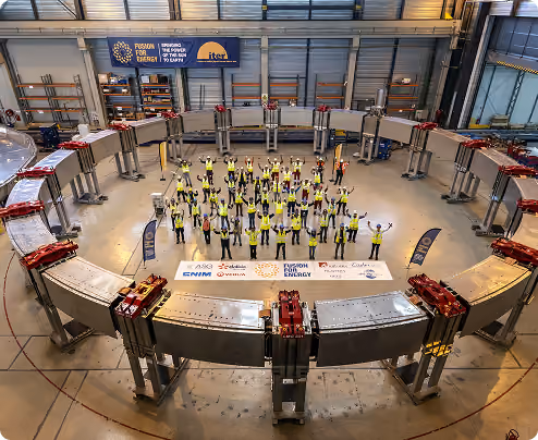 Group of people in safety vests standing inside a large circular metal structure in an industrial space.