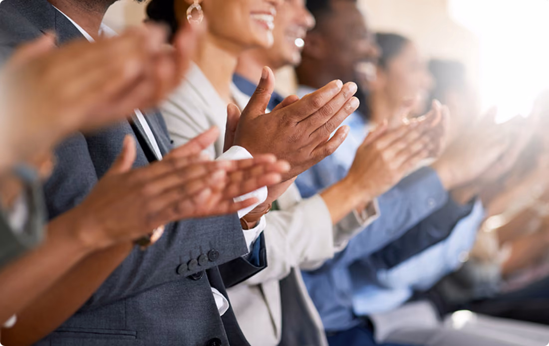 Diverse group of people in business attire applauding, seated in a row.