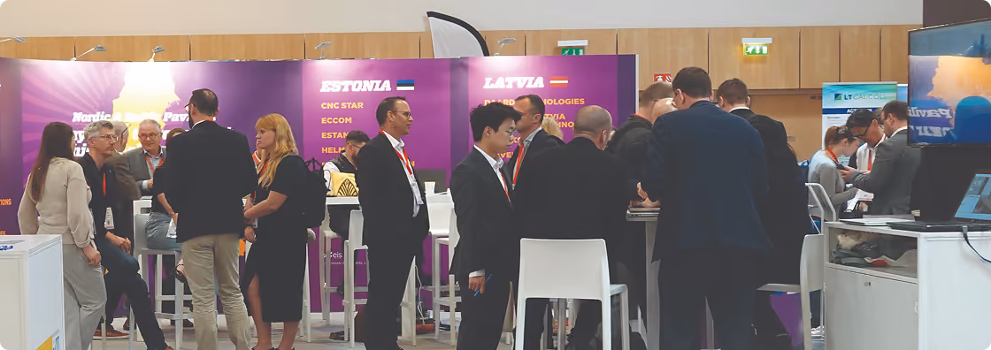 People networking and conversing at a trade show booth with Estonia and Latvia company displays.