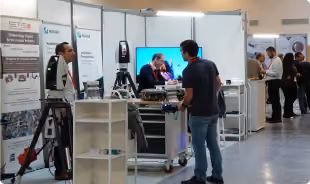 People interacting at a technology booth in a convention or exhibition hall with various equipment on display.